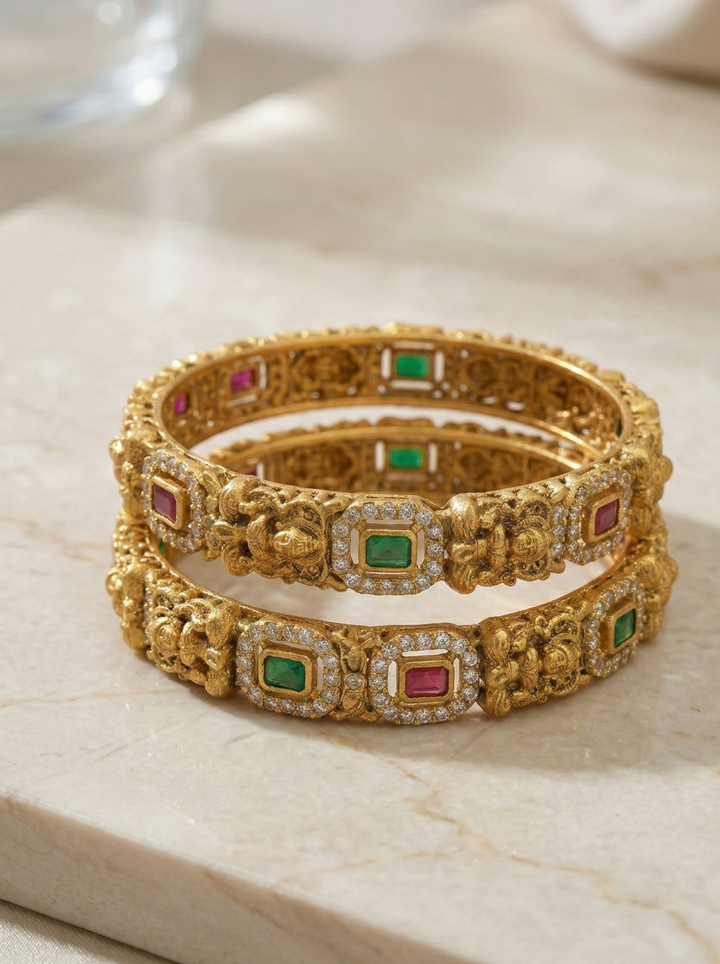 Two gold bangles with gemstones on a light marble surface