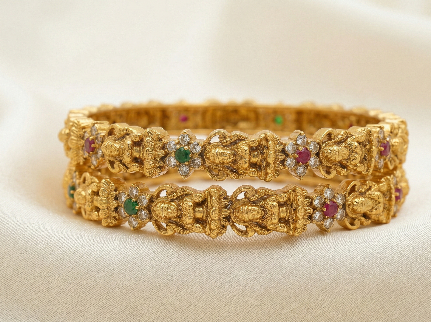 Pair of gold bangles with gemstone accents on a beige background