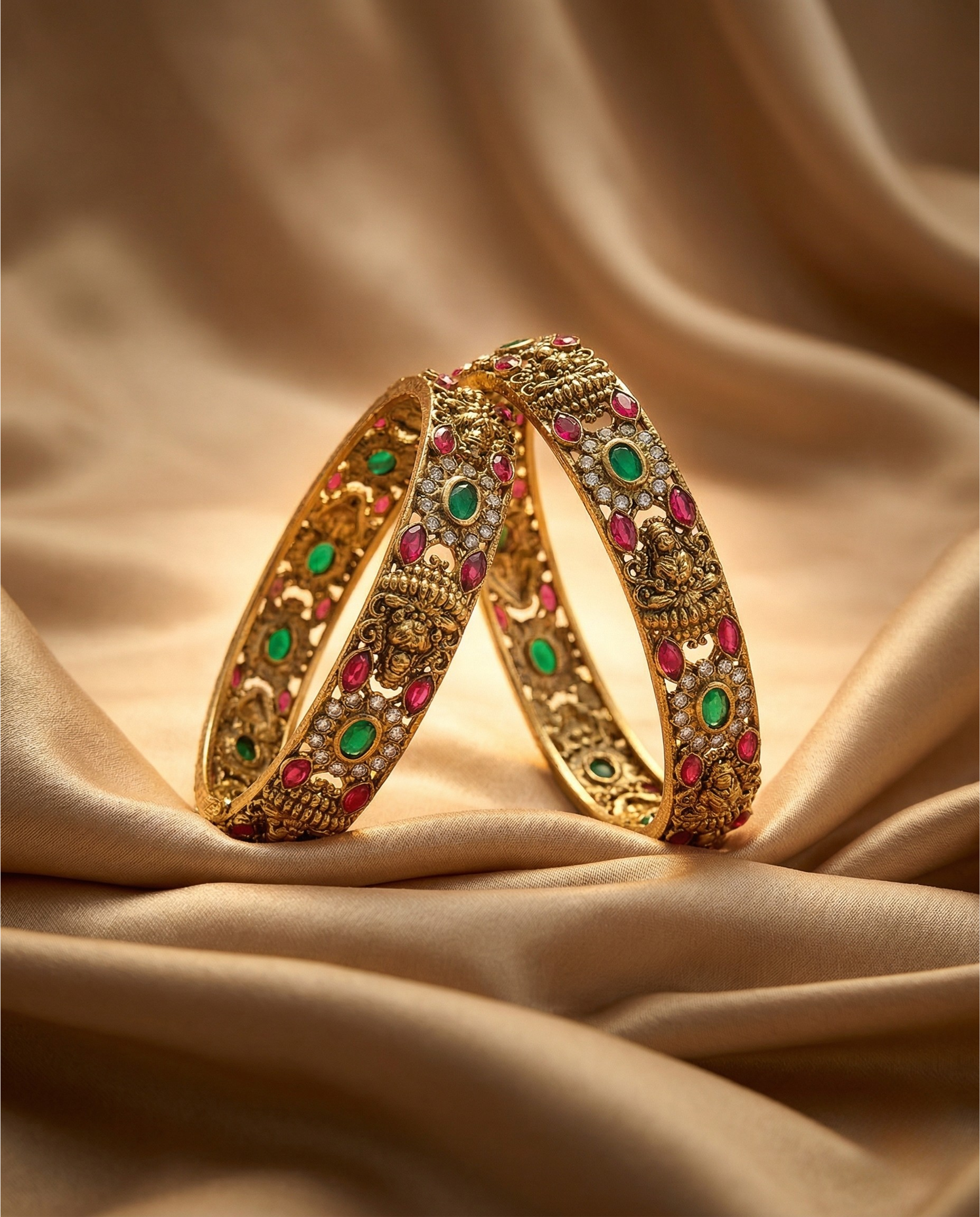 Pair of gold bangles with gemstones on a beige fabric background