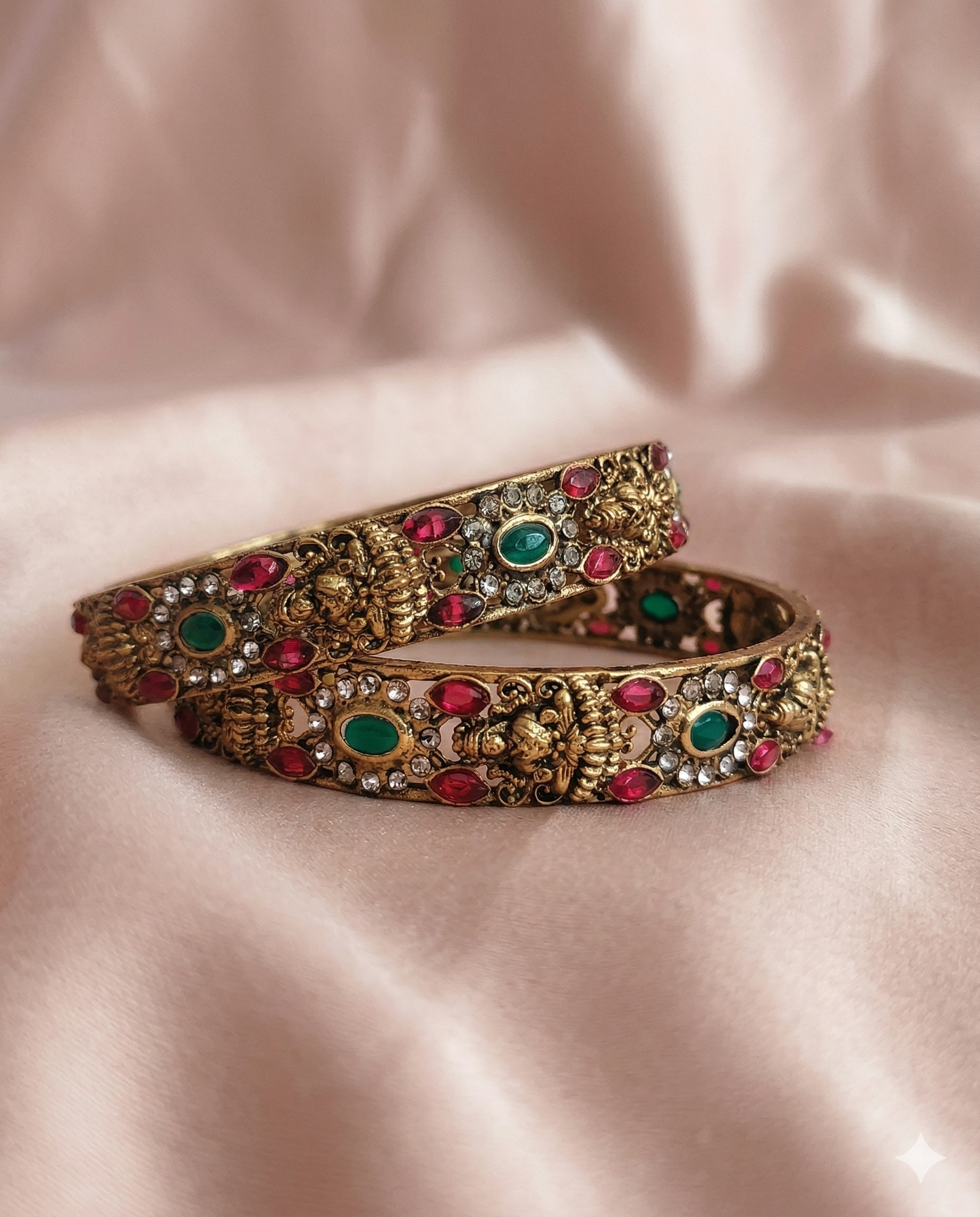 Decorative bracelet with gold, red, and green stones on a pink satin background