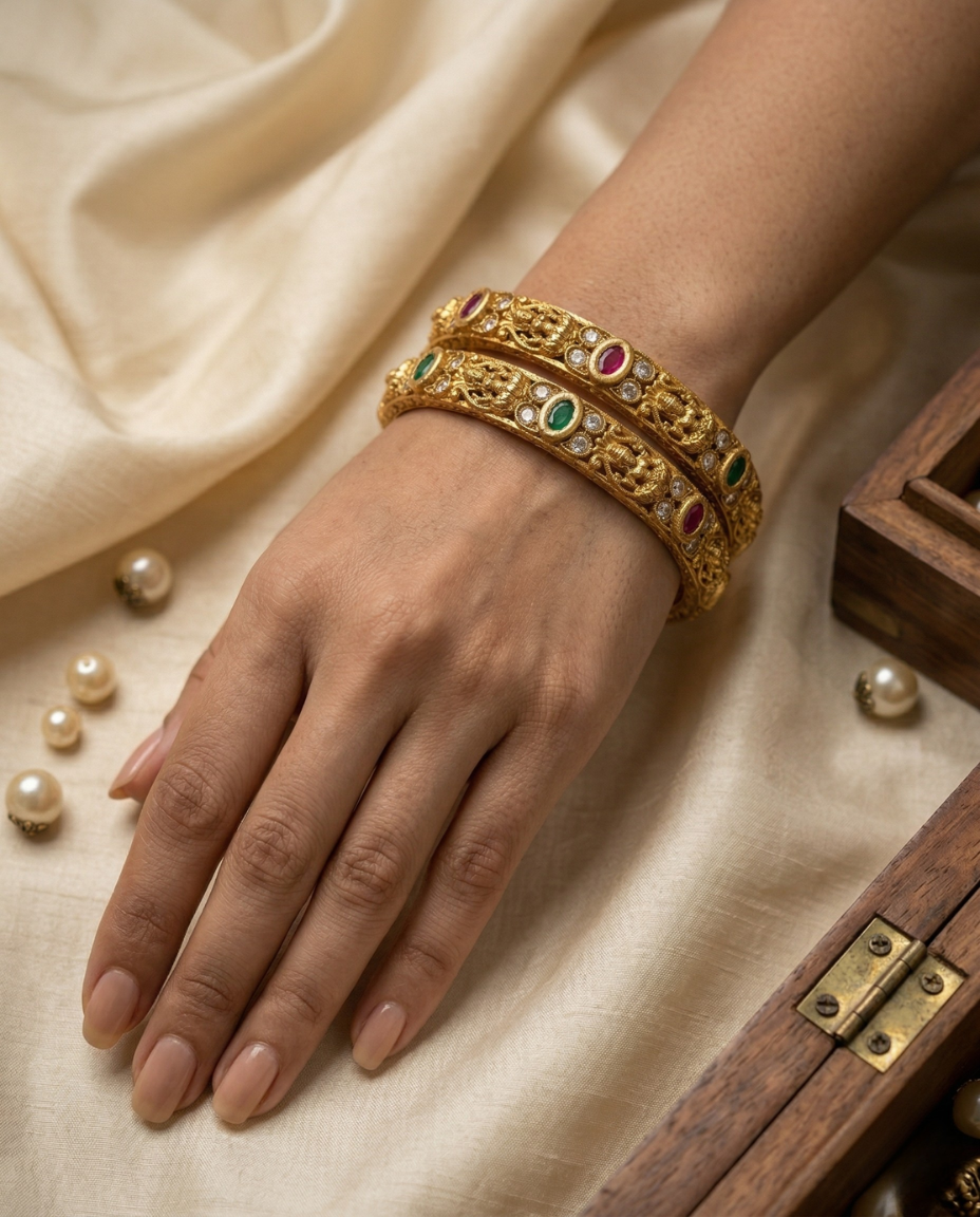 Gold bracelet with gemstones on a hand, placed on a beige fabric background with pearls and a wooden box.