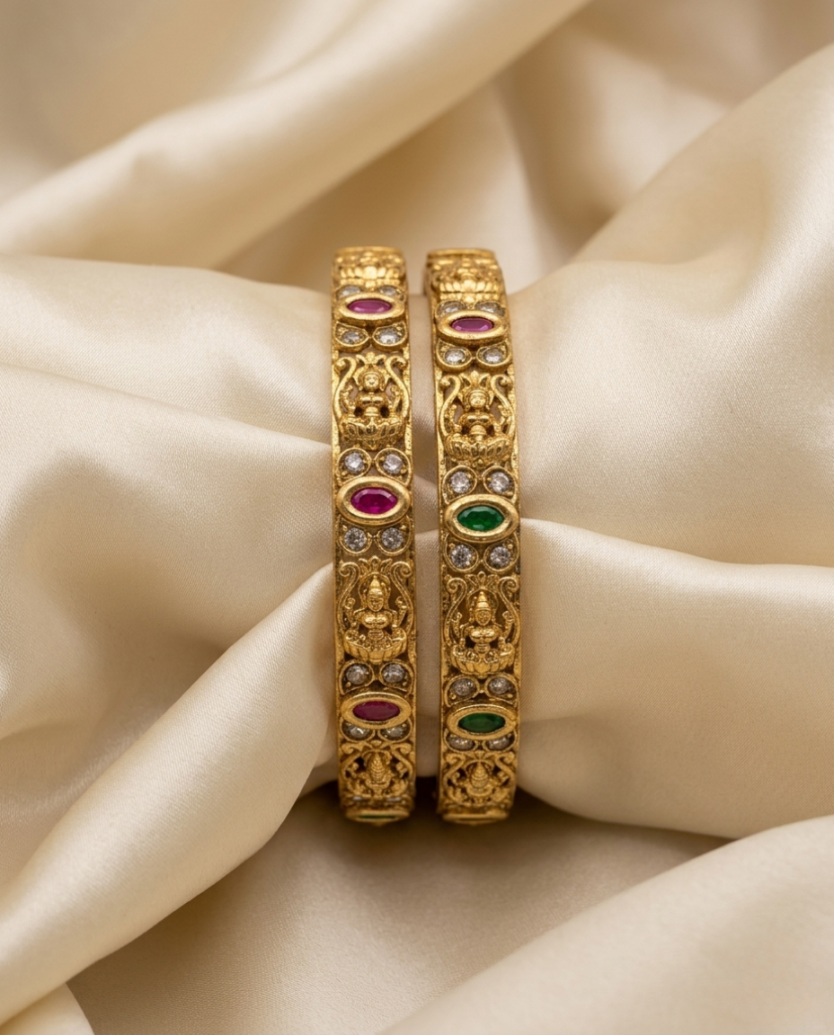 Two gold bangles with gemstones on a beige fabric background