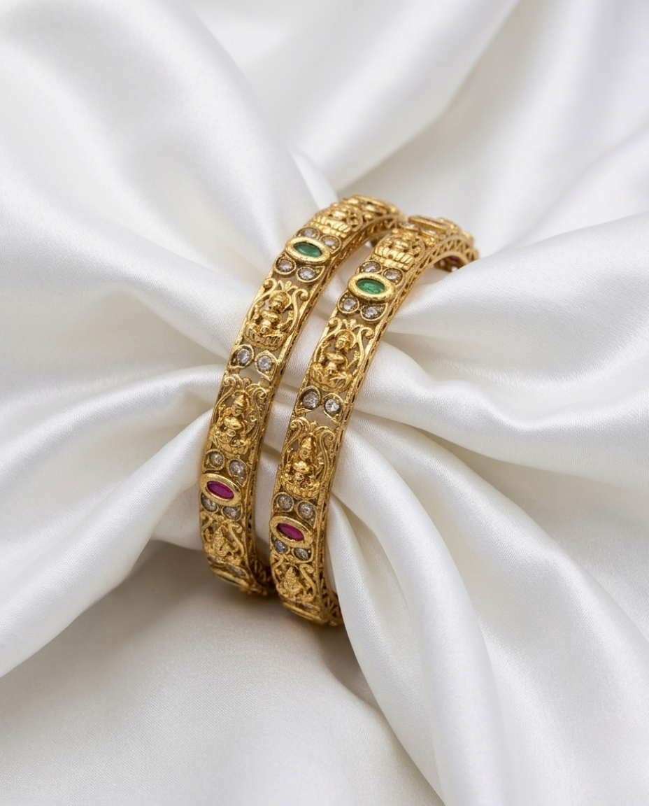 Two gold bangles with gemstones on a white fabric background