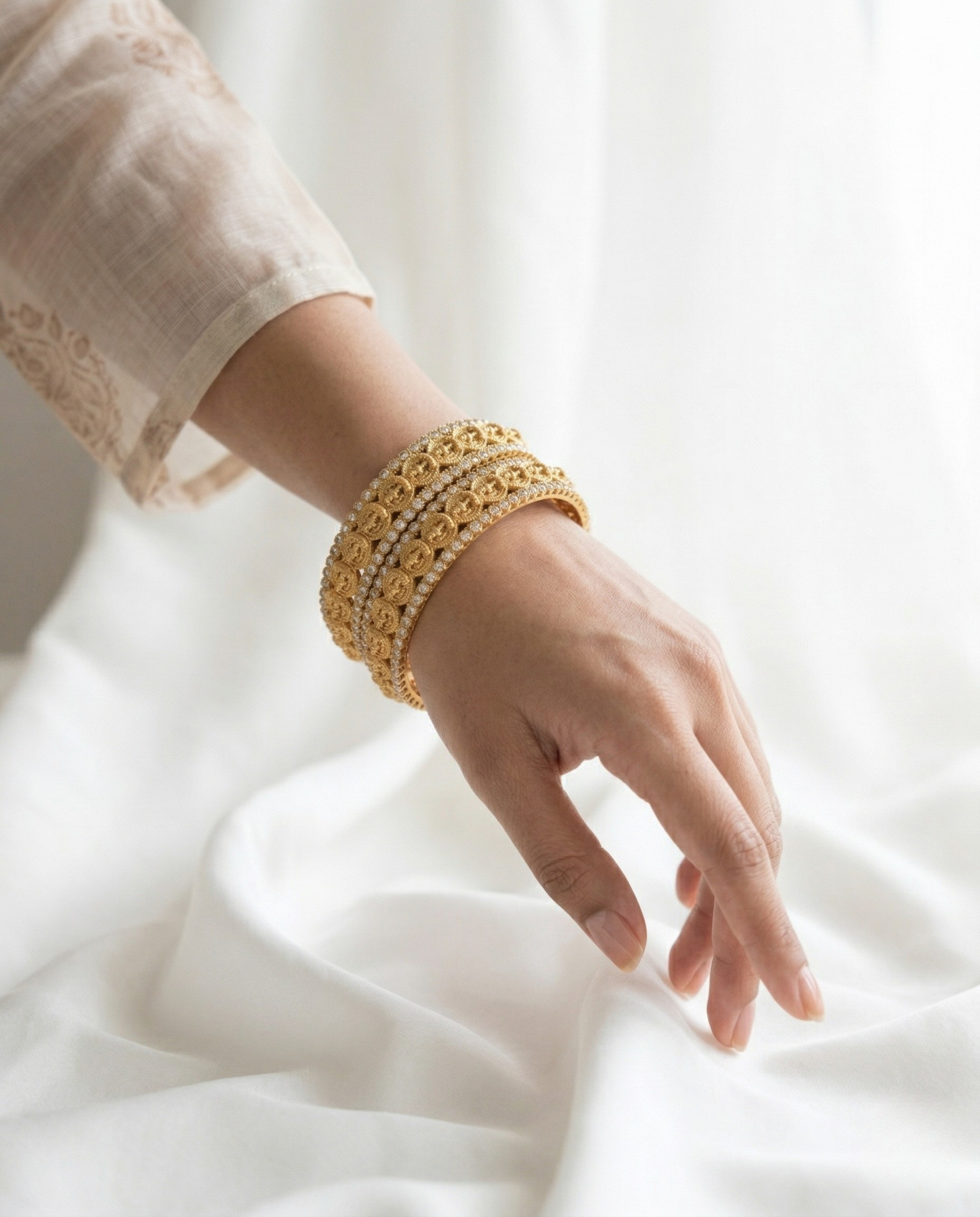 Hand wearing a gold bracelet on a white fabric background