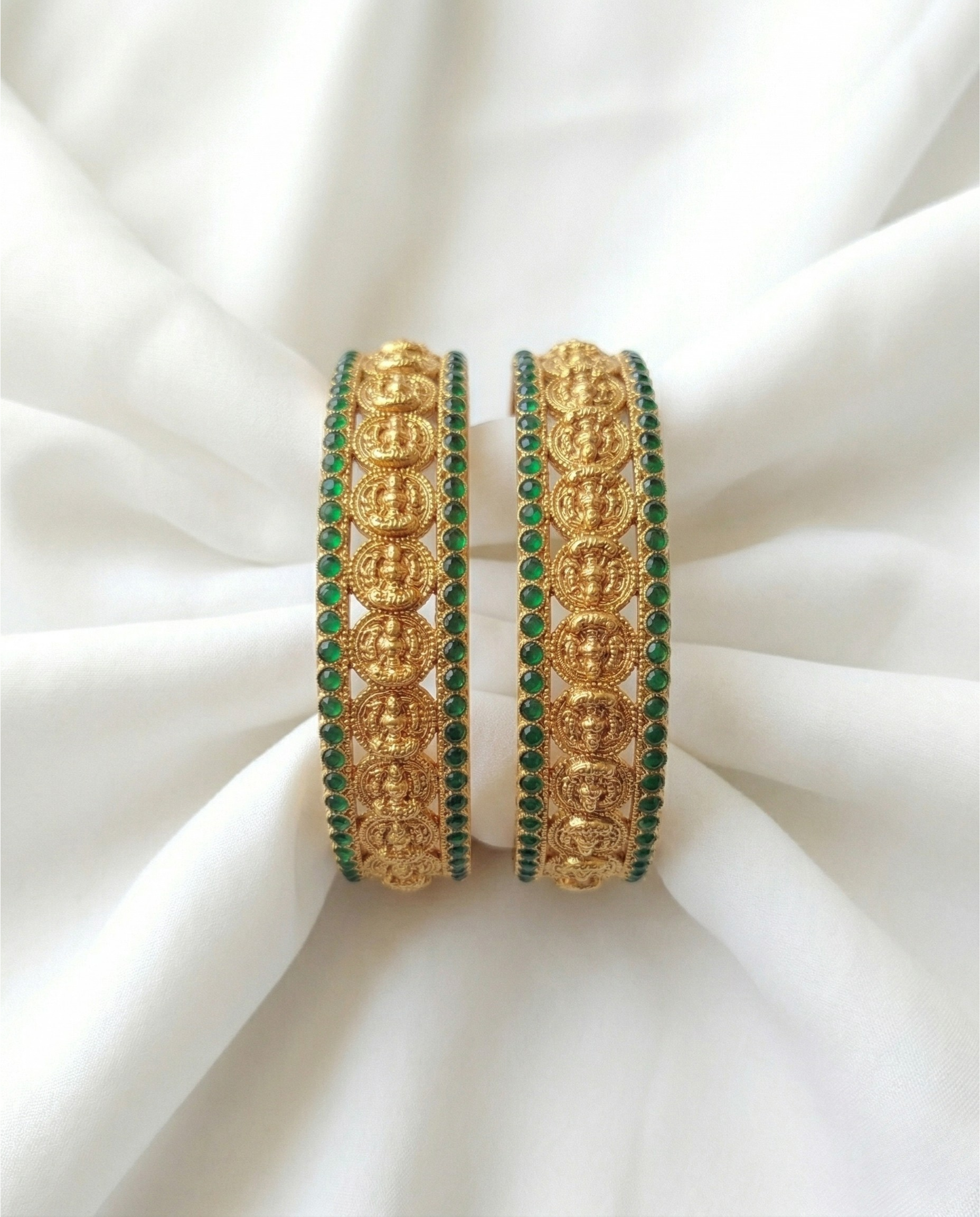 Pair of gold and green bangles on a white fabric background