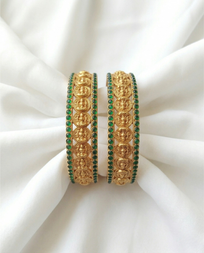 Pair of gold and green bangles on a white fabric background
