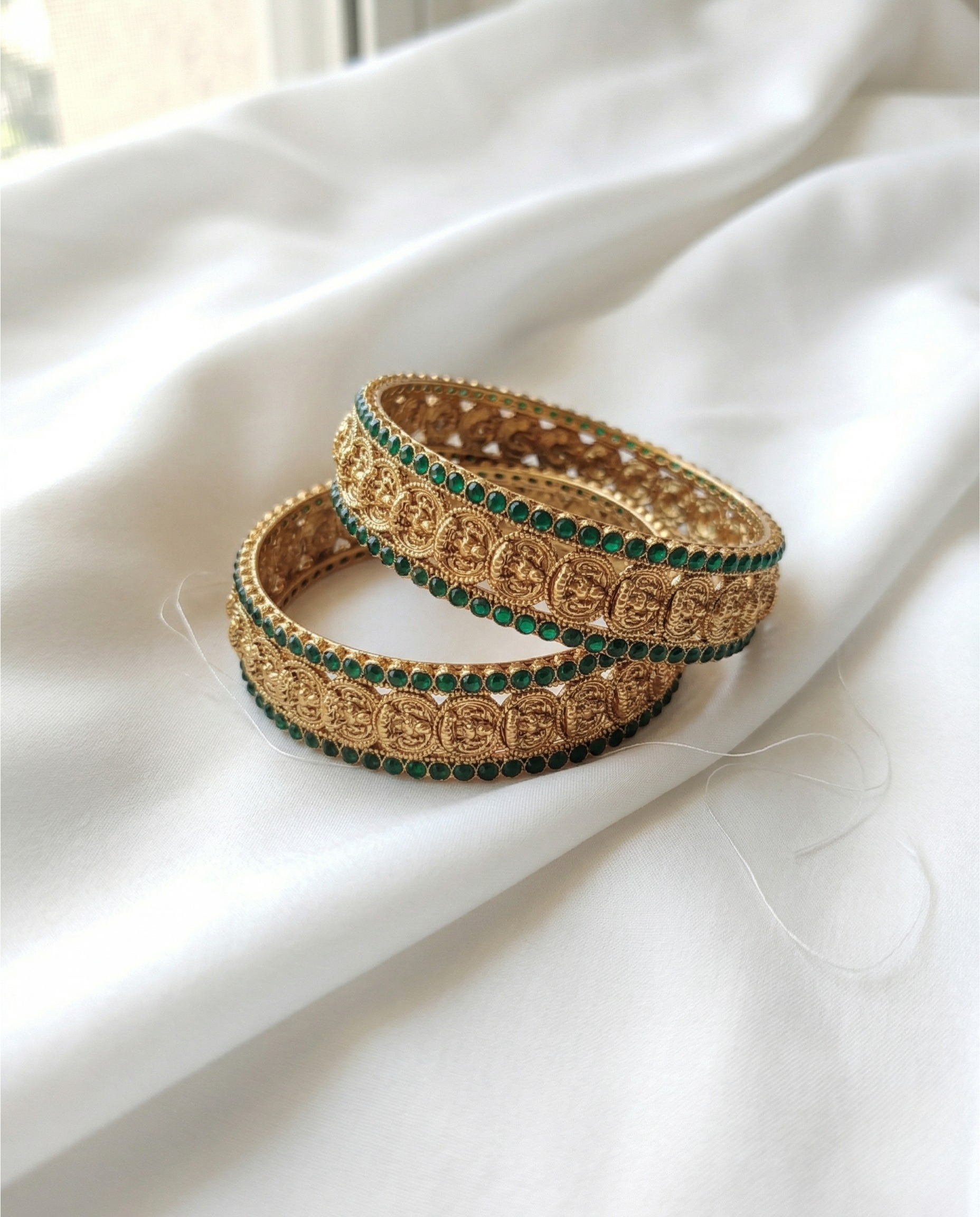 Gold and green bangles on a white fabric background