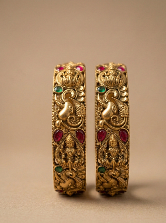 Pair of ornate gold bangles with gemstones on a beige background