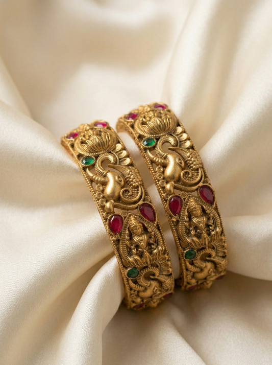 Gold bangles with red and green stones on a beige fabric background