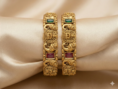 Pair of gold bangles with gemstones on a beige fabric background
