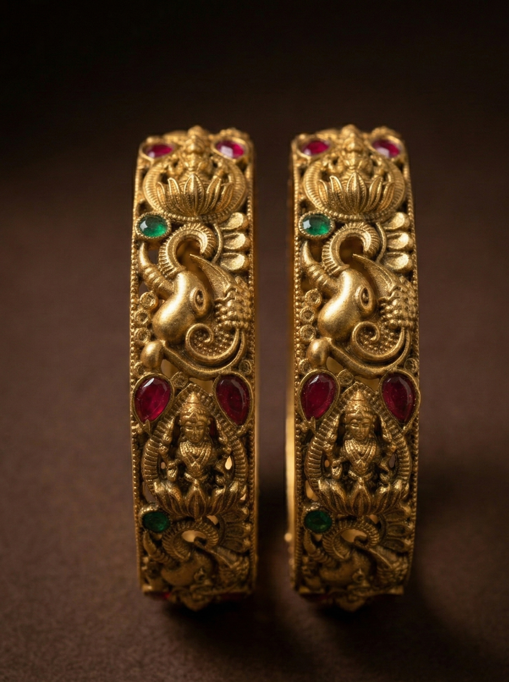 Pair of ornate gold earrings with red and green gemstones on a dark background