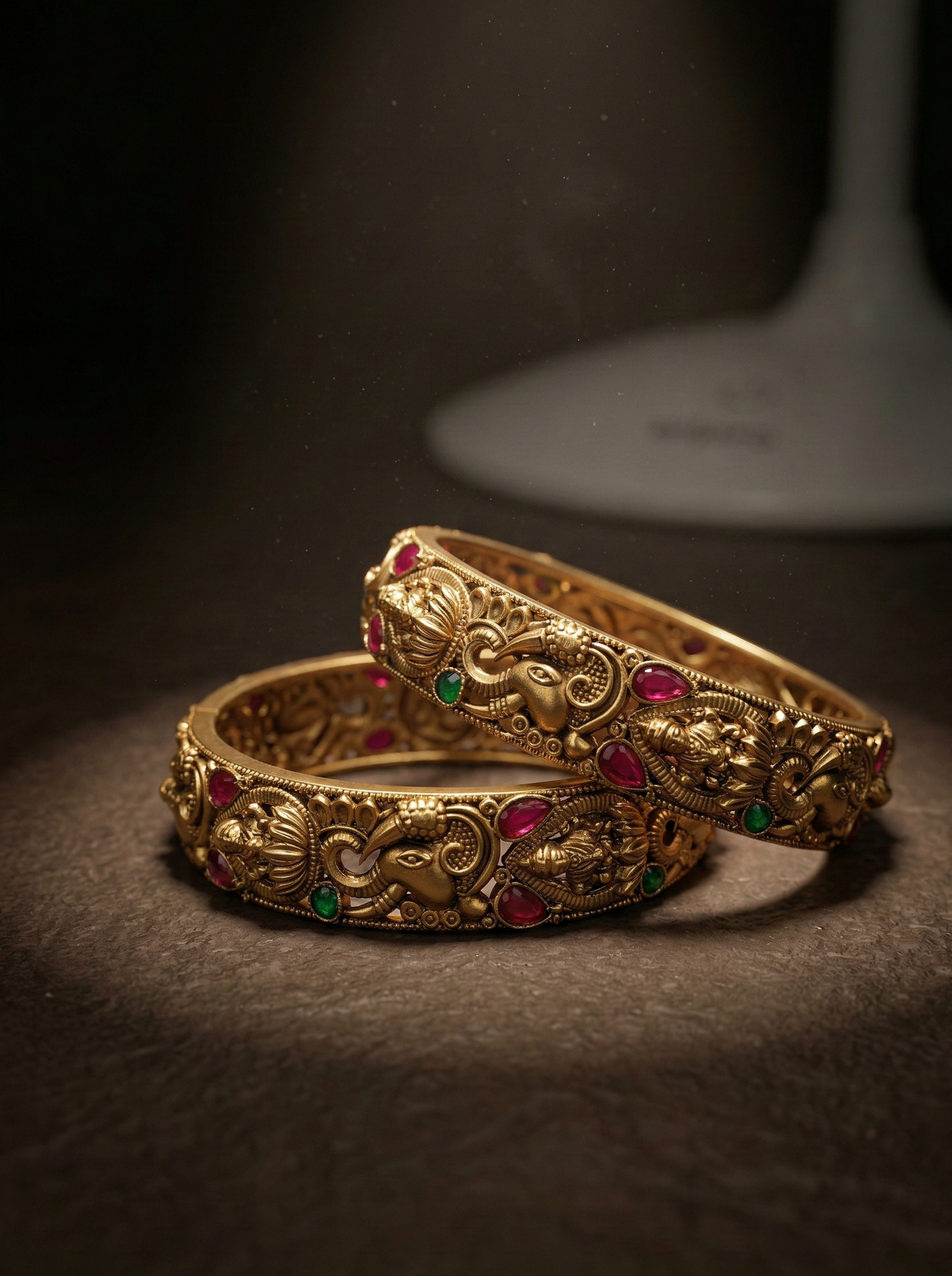 Pair of ornate gold bangles with gemstones on a dark background