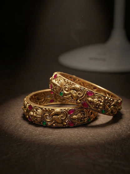Pair of ornate gold bangles with gemstones on a dark background