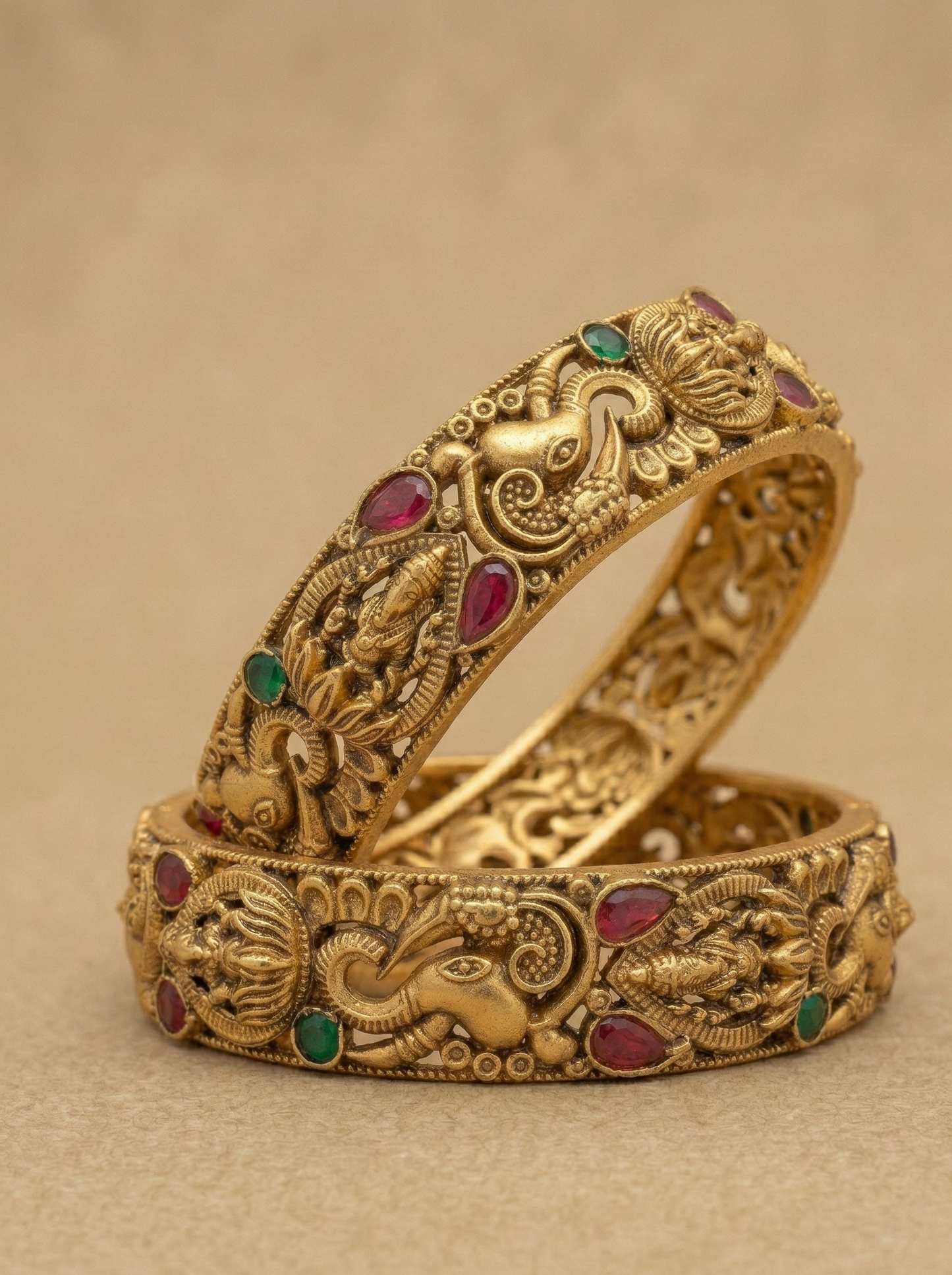 Gold bangles with intricate designs and gemstones on a beige background