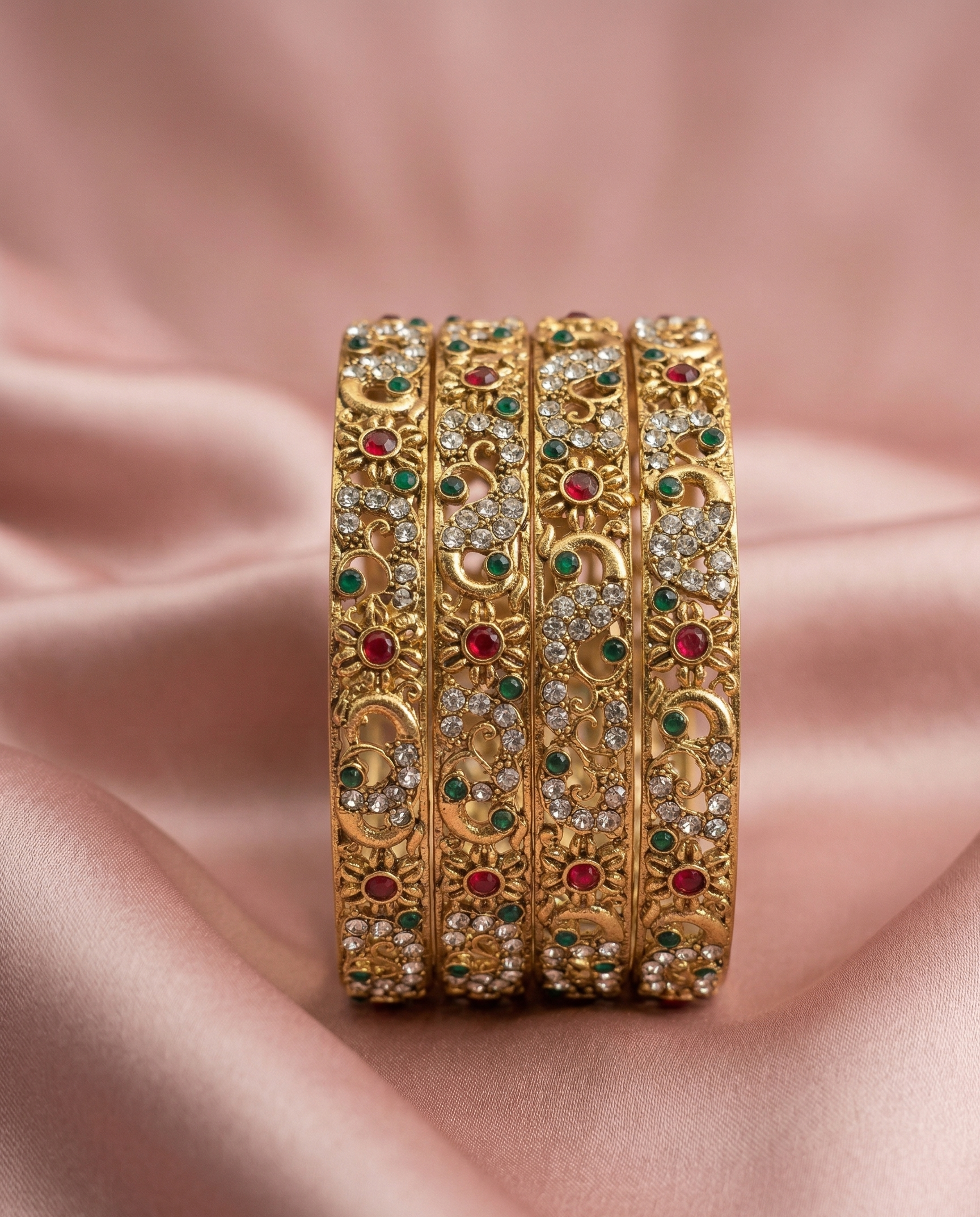 Set of gold bangles with gemstones on a pink fabric background