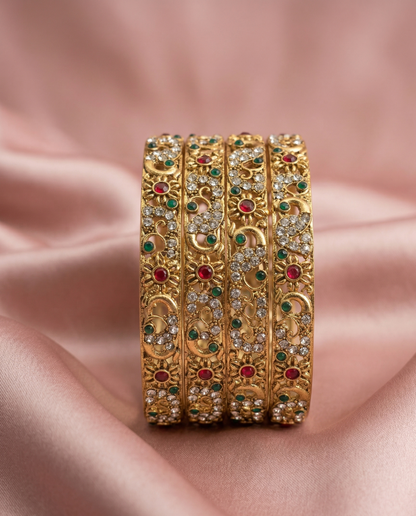 Set of gold bangles with gemstones on a pink fabric background