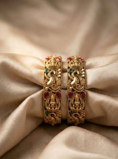 Pair of gold bangles with gemstones on a beige fabric background