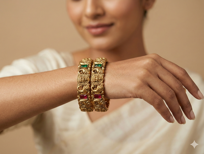 Gold bangles with gemstones on a person's wrist against a neutral background