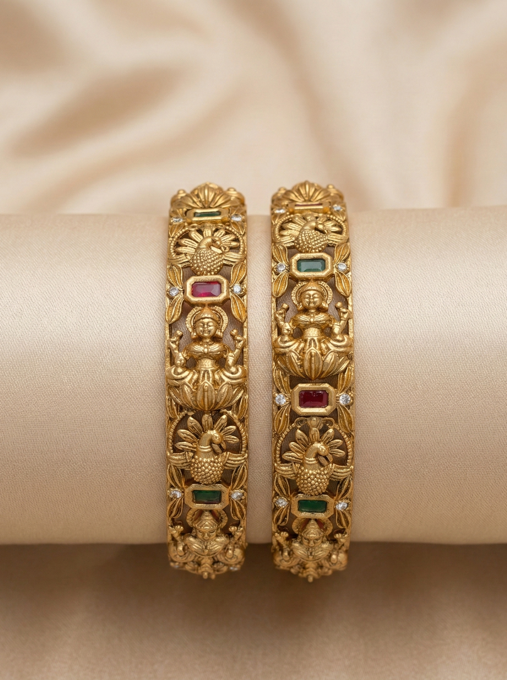 Pair of ornate gold bangles with gemstones on a beige fabric background