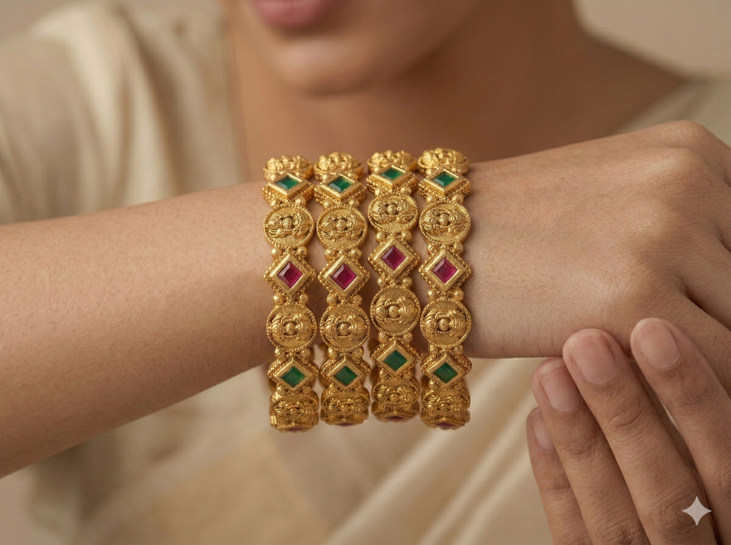 Gold bangles with gemstones on a wrist against a neutral background