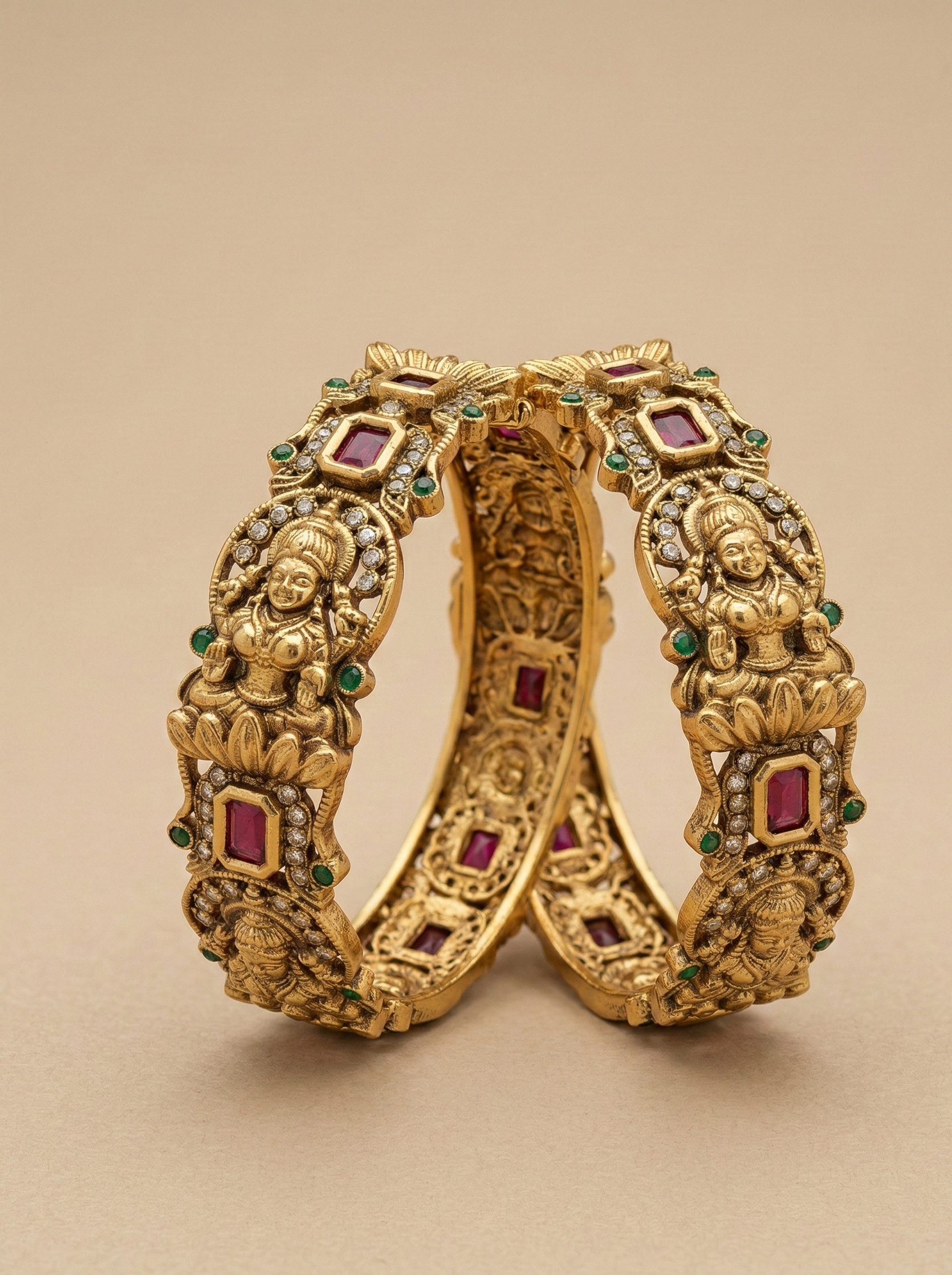 Gold bangles with intricate designs and gemstones on a beige background