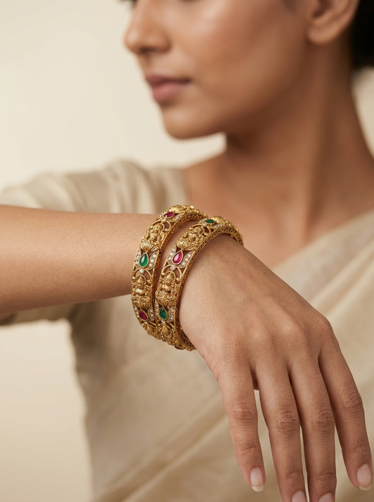 Close-up of a person wearing a gold bracelet with gemstones on a neutral background