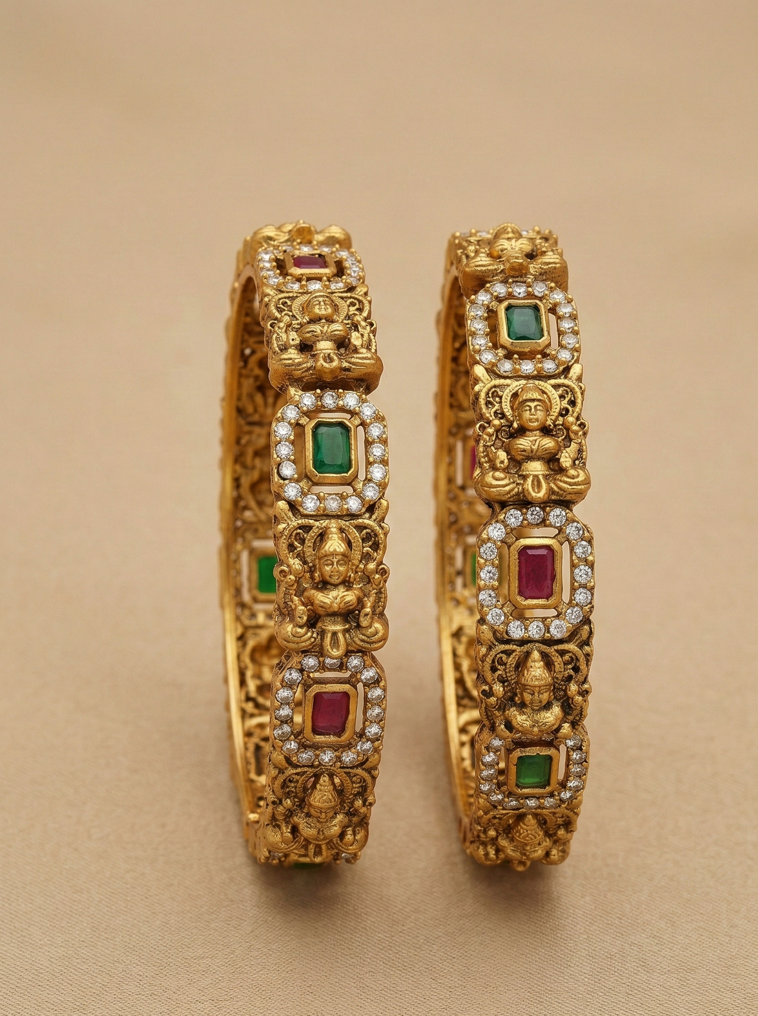 Pair of gold bangles with gemstones on a beige background