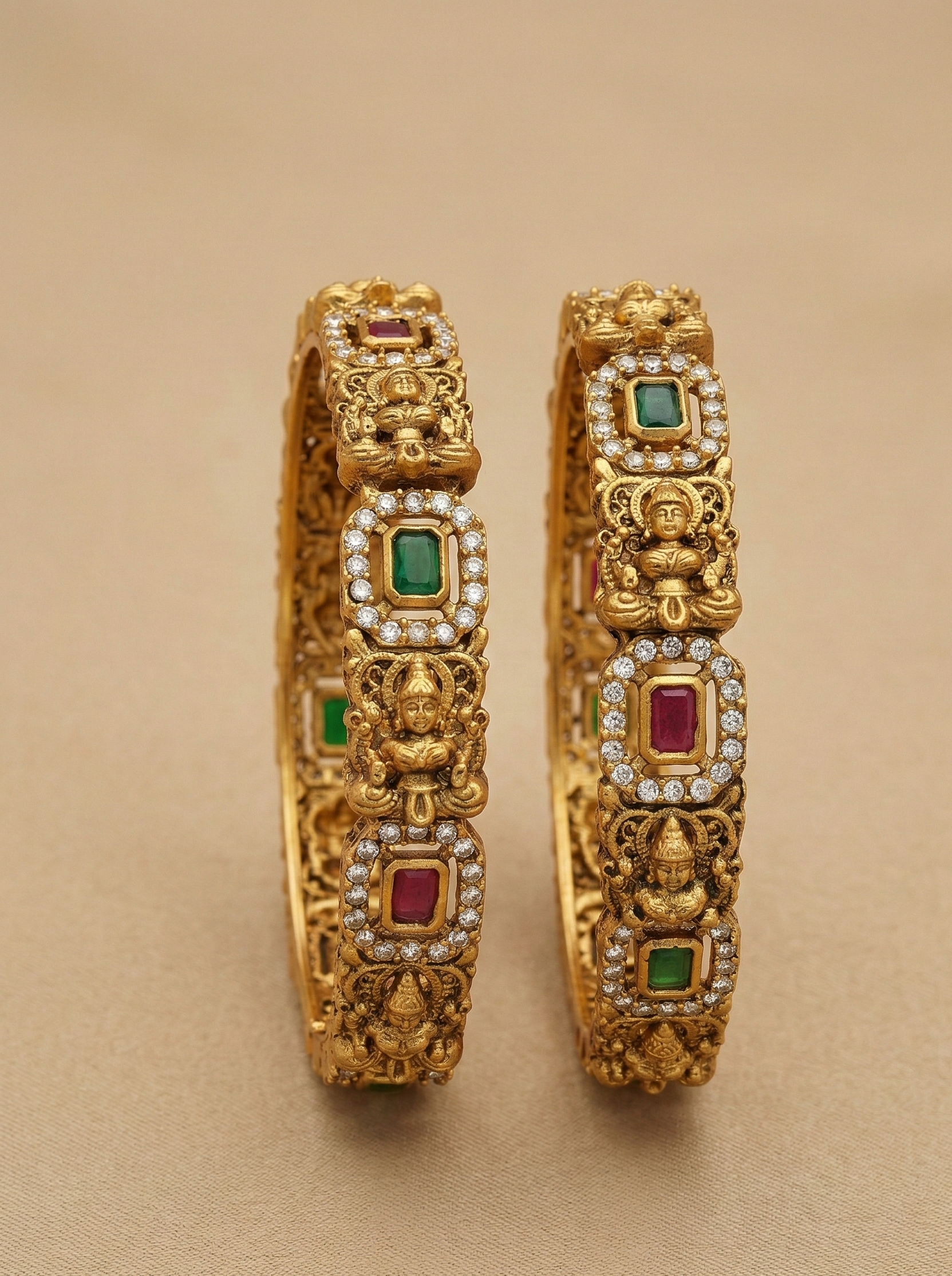 Pair of gold bangles with gemstones on a beige background