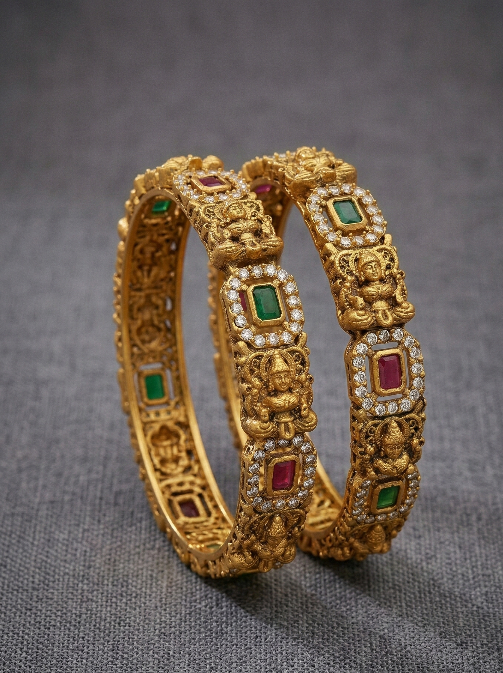 Pair of gold bangles with gemstone inlays on a gray background