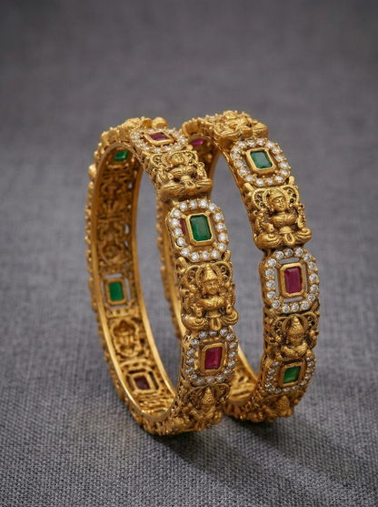 Pair of gold bangles with gemstone inlays on a gray background