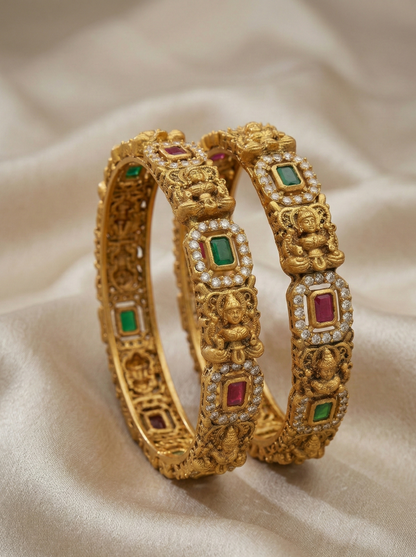 Pair of gold bangles with gemstones on a beige fabric background