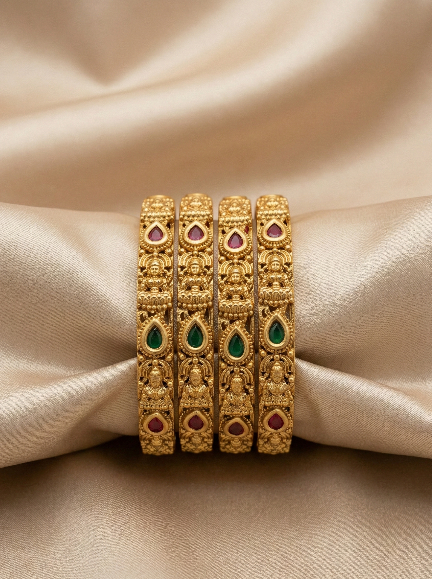 Set of gold bangles with gemstones on a beige fabric background