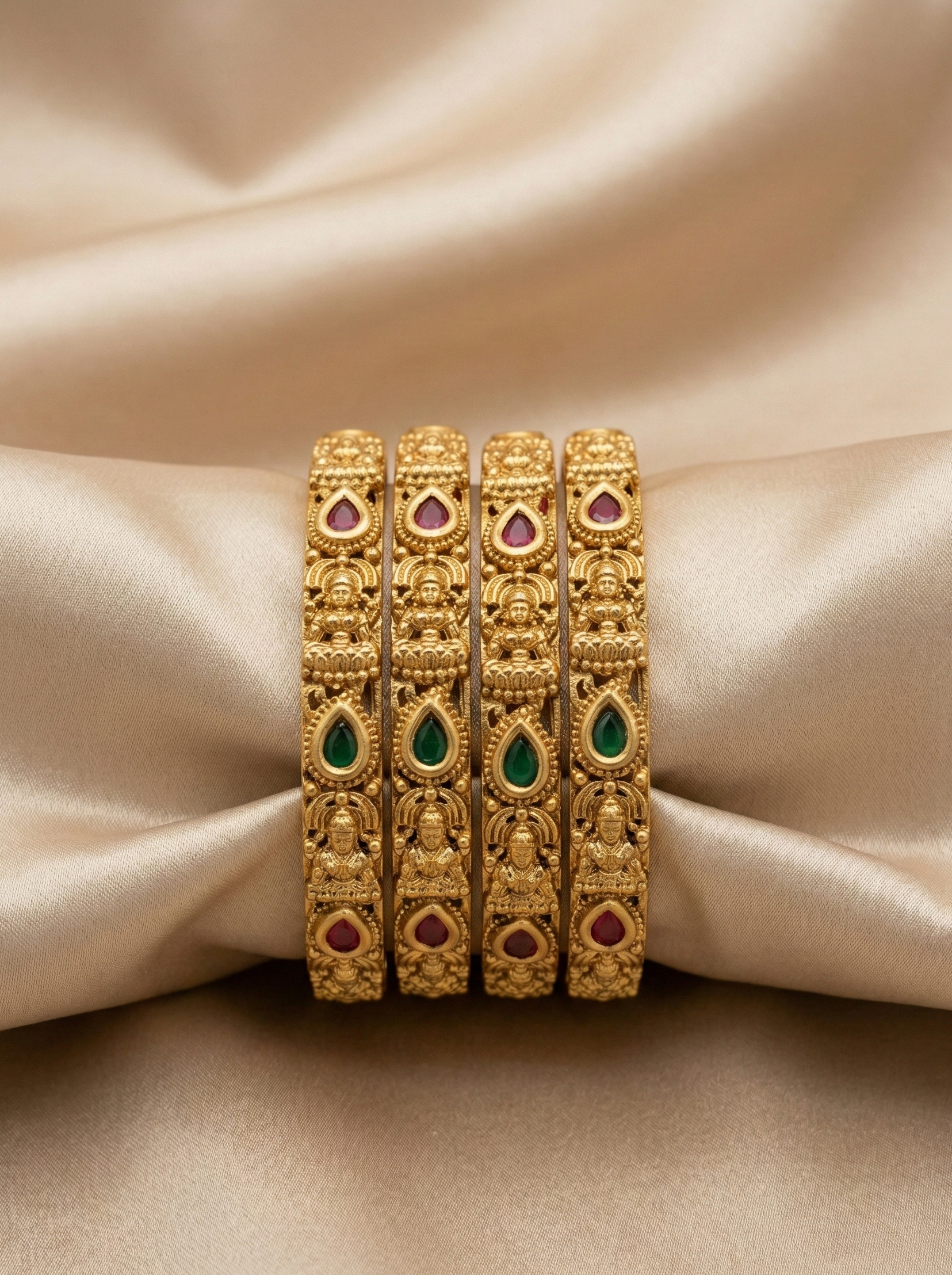 Set of gold bangles with gemstones on a beige fabric background