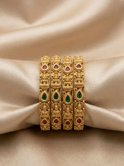 Set of gold bangles with gemstones on a beige fabric background