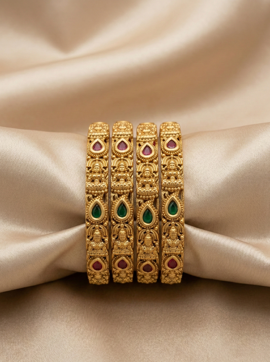 Set of gold bangles with gemstones on a beige fabric background
