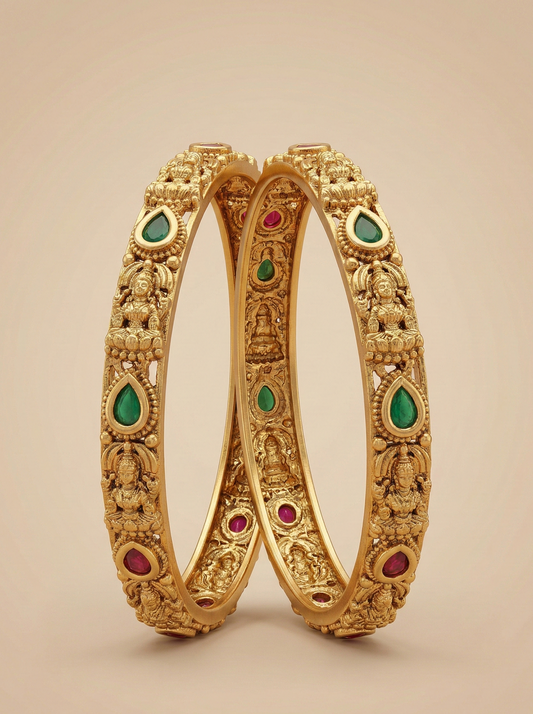 Pair of gold bangles with green and red gemstones on a beige background