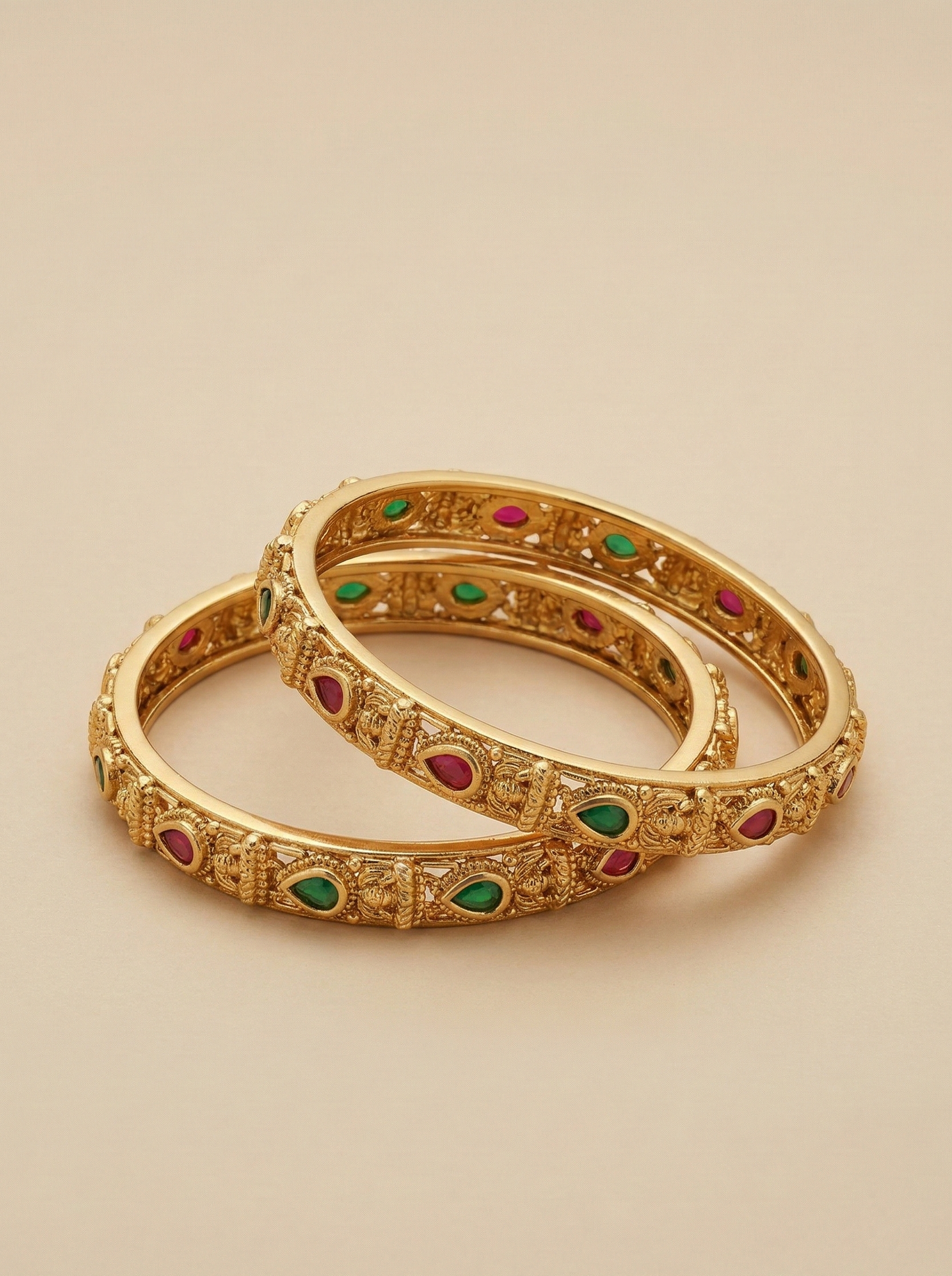 Pair of gold bangles with gemstone accents on a beige background
