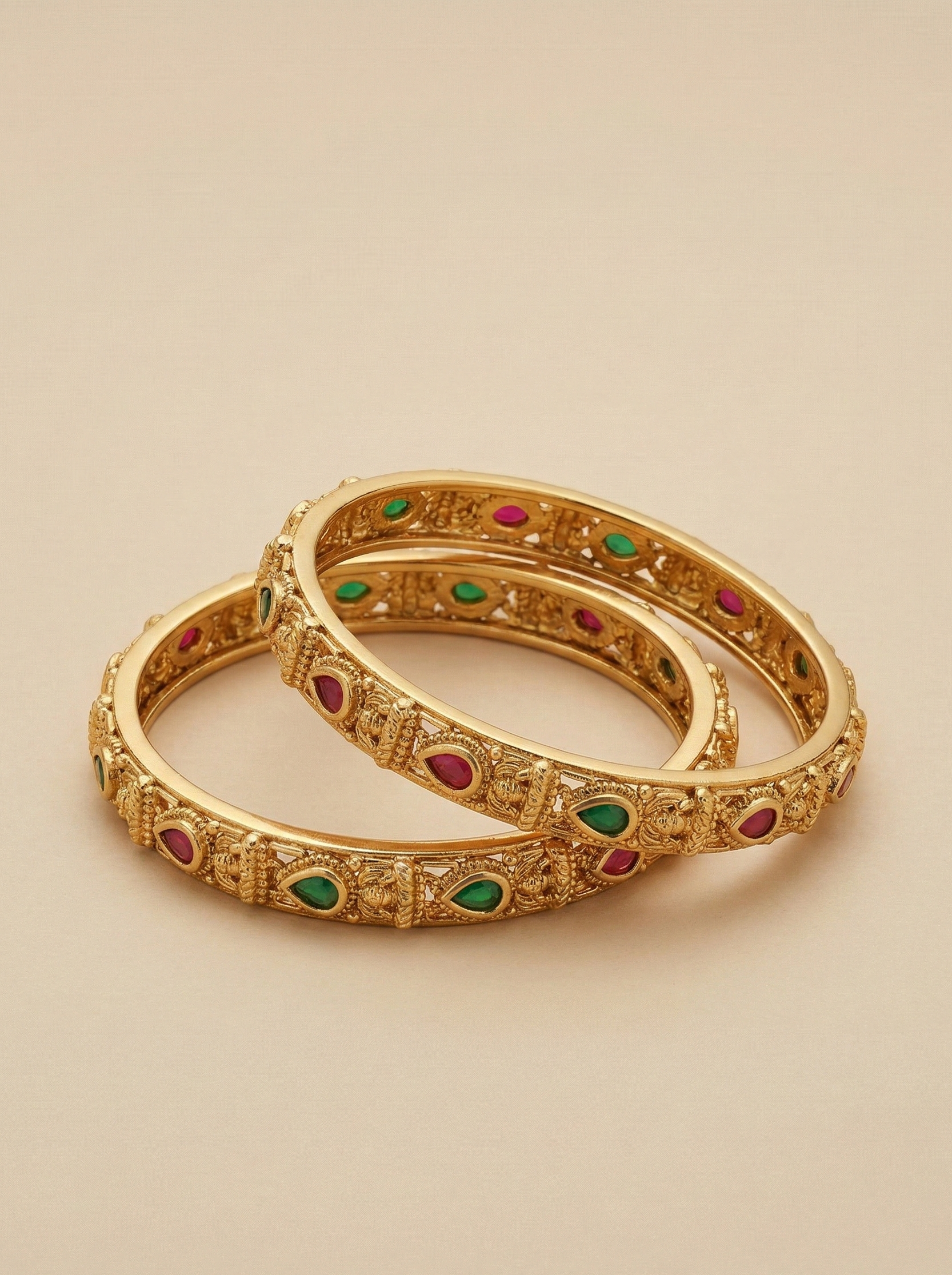 Pair of gold bangles with gemstone accents on a beige background