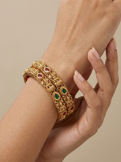 Gold bracelet with gemstones on a wrist against a beige background