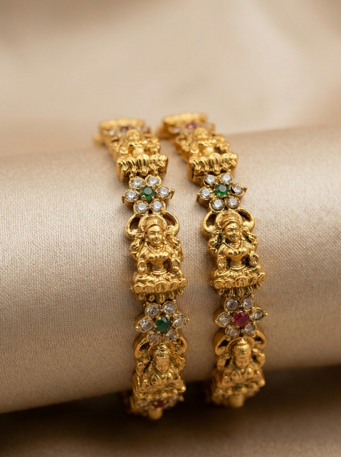 Gold earrings with intricate designs and gemstones on a beige fabric background