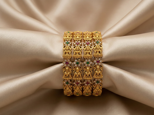 Pair of gold bangles with gemstone accents on a beige background