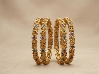 Pair of gold bangles with gemstones on a beige background