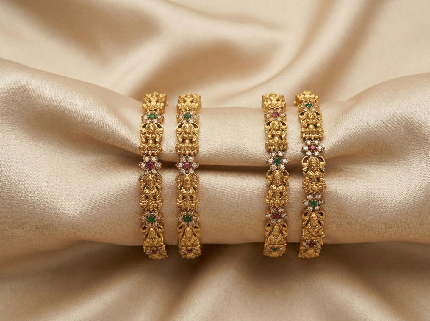 Set of gold bangles with gemstones on a beige fabric background