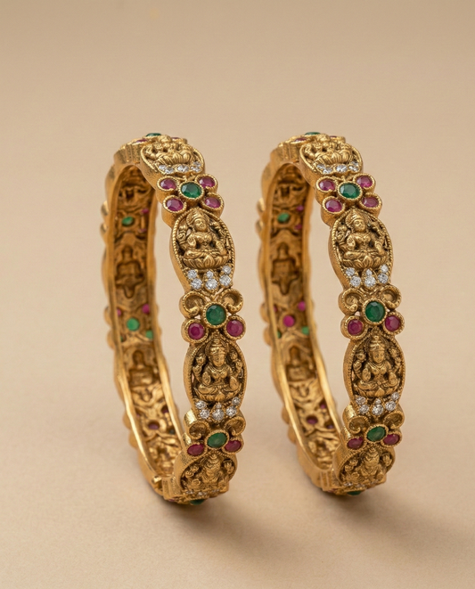 Pair of ornate gold bangles with gemstones on a beige background