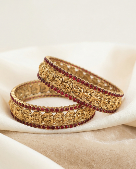 Pair of gold and red beaded bracelets on a beige fabric background