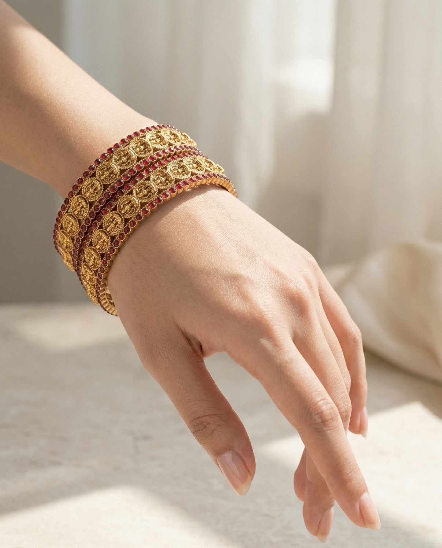 Hand wearing a gold bracelet with red stones on a light background