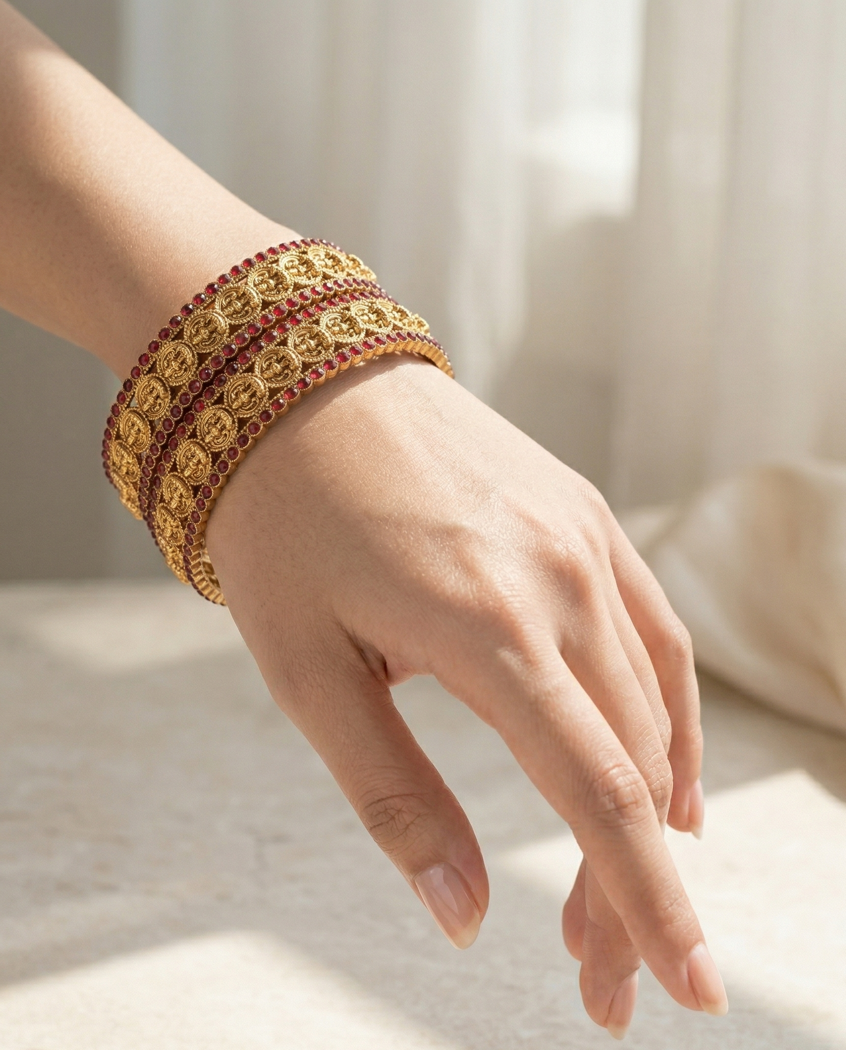 Hand wearing a gold bracelet with red stones on a light background