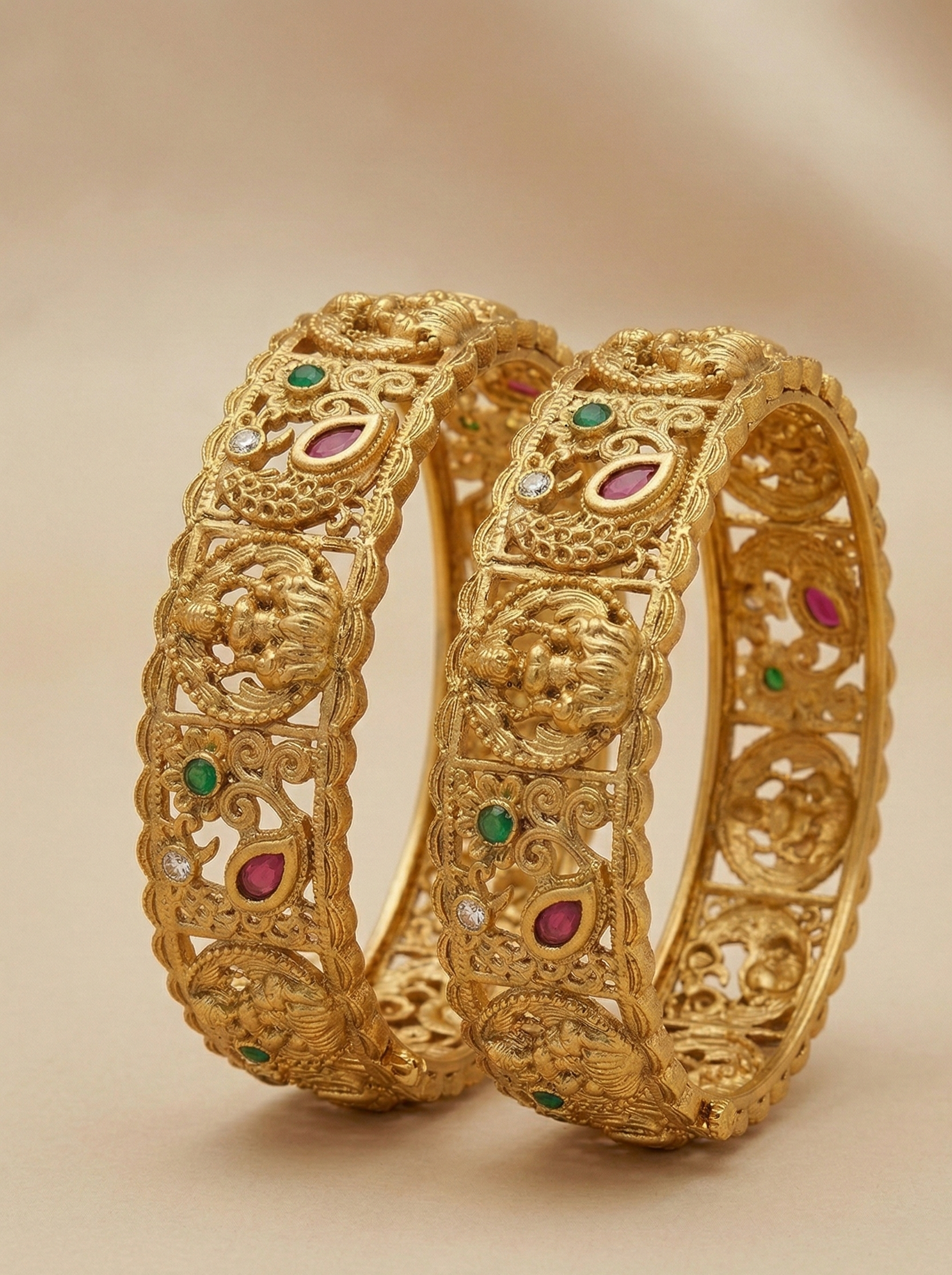 Pair of gold bangles with gemstone inlays on a beige background