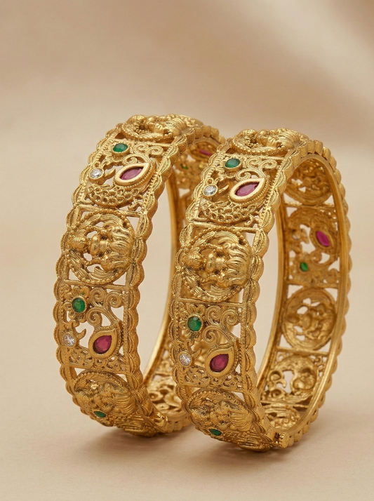 Pair of gold bangles with gemstone inlays on a beige background