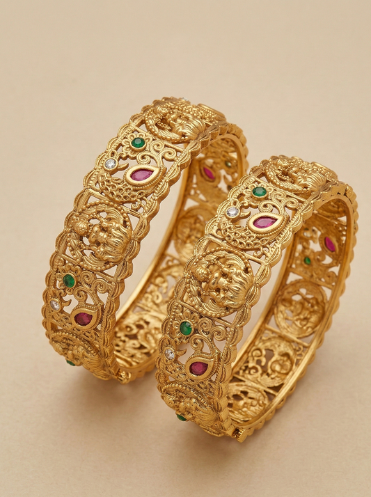 Pair of gold bangles with gemstone accents on a beige background